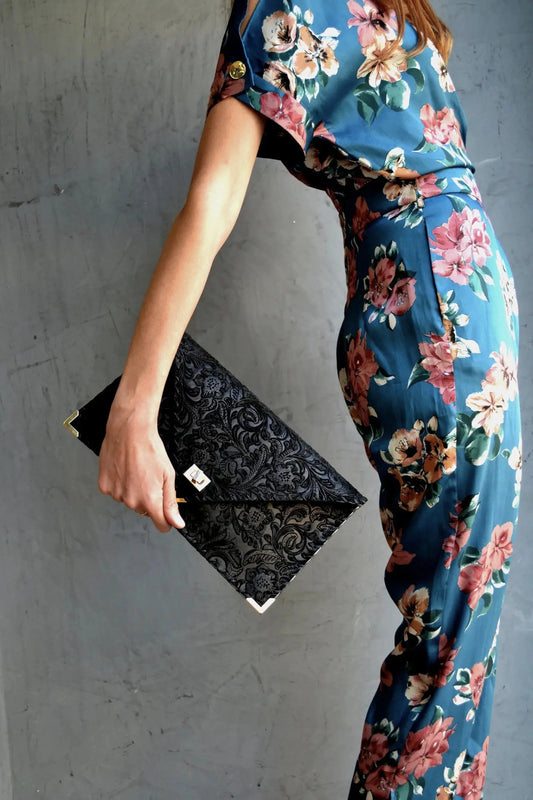 A model in a floral pantsuit holding the Symmetria Floral All Day Leather Clutch behind her back. 