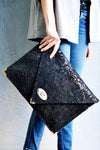 Symmetria Floral Leather Large Clutch i black held by a woman wearing jeans